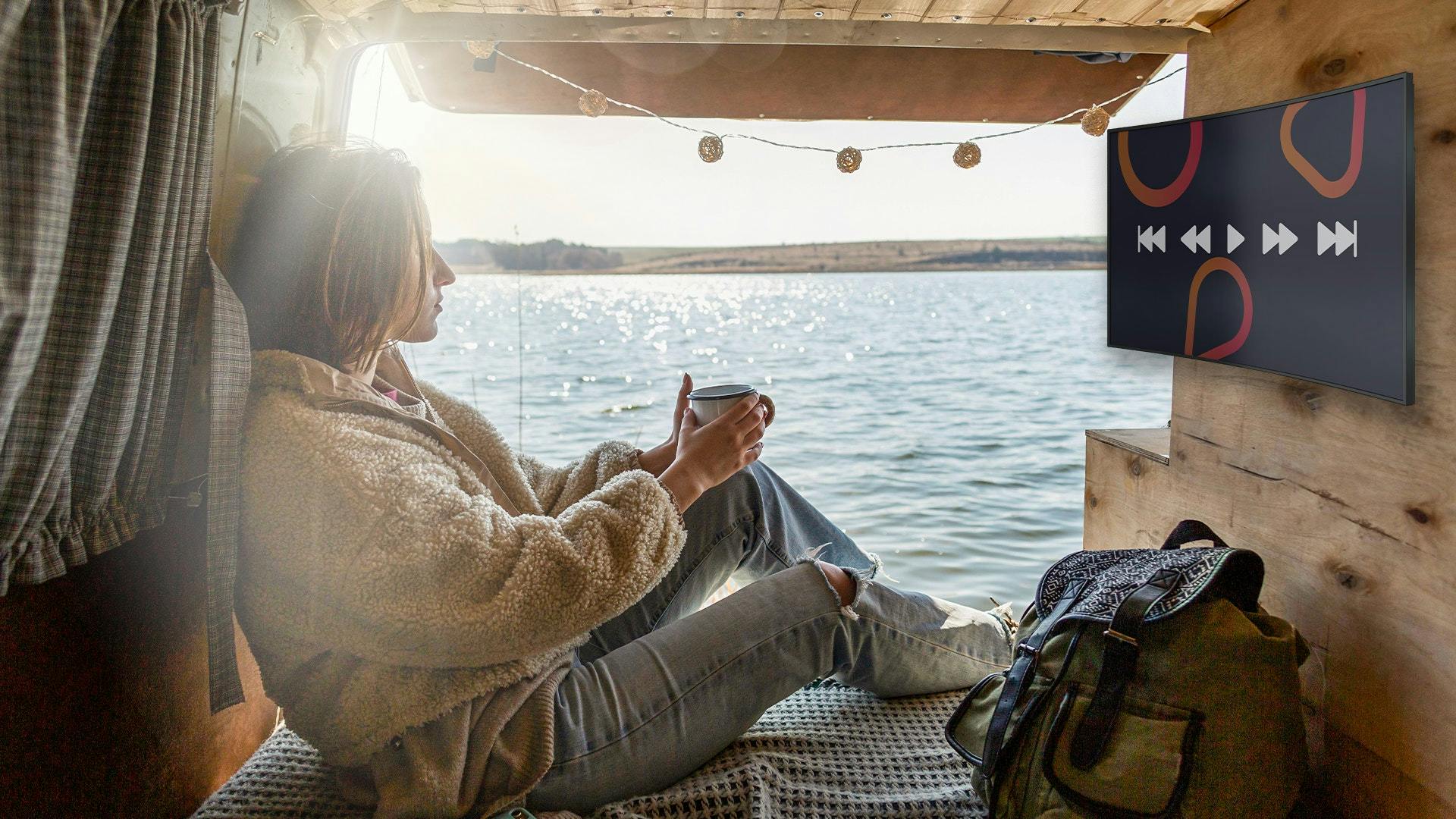 Frau mit einer Tasse in der Hand sitzt in einem Van am Meer