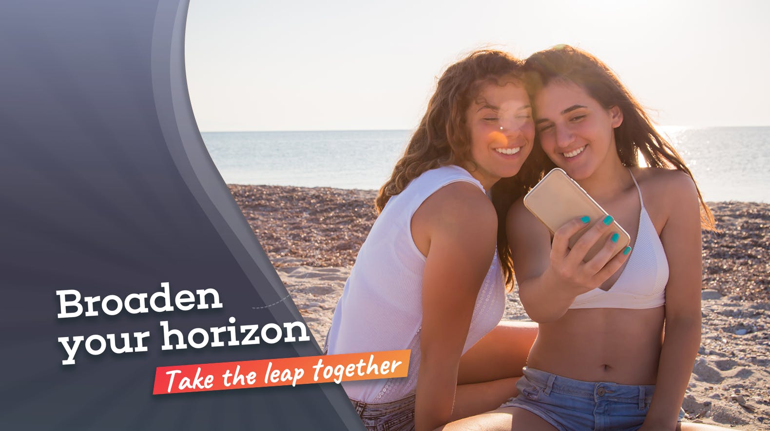 Twee meiden op het strand, waarvan de een de ander iets op een telefoon laat zien met de slogan 'Broaden your horizon'