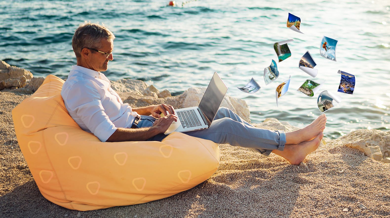 Mann sitz mit seinem Laptop auf einem Sitzsack am Strand aus dem kleine Bilder fliegen