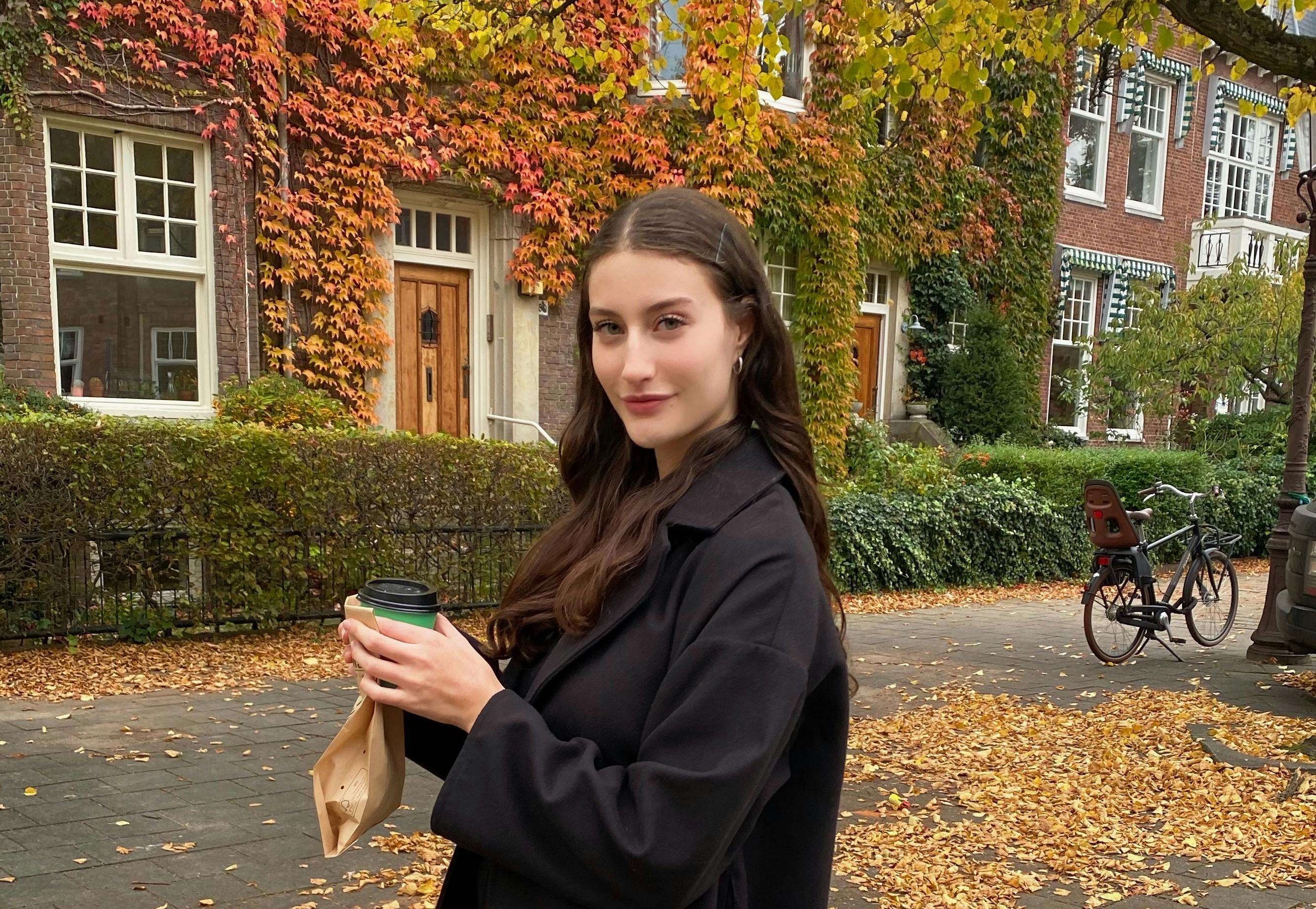 Mädchen in Amsterdam und im Hintergrund ein Haus und Bäume im Herbst