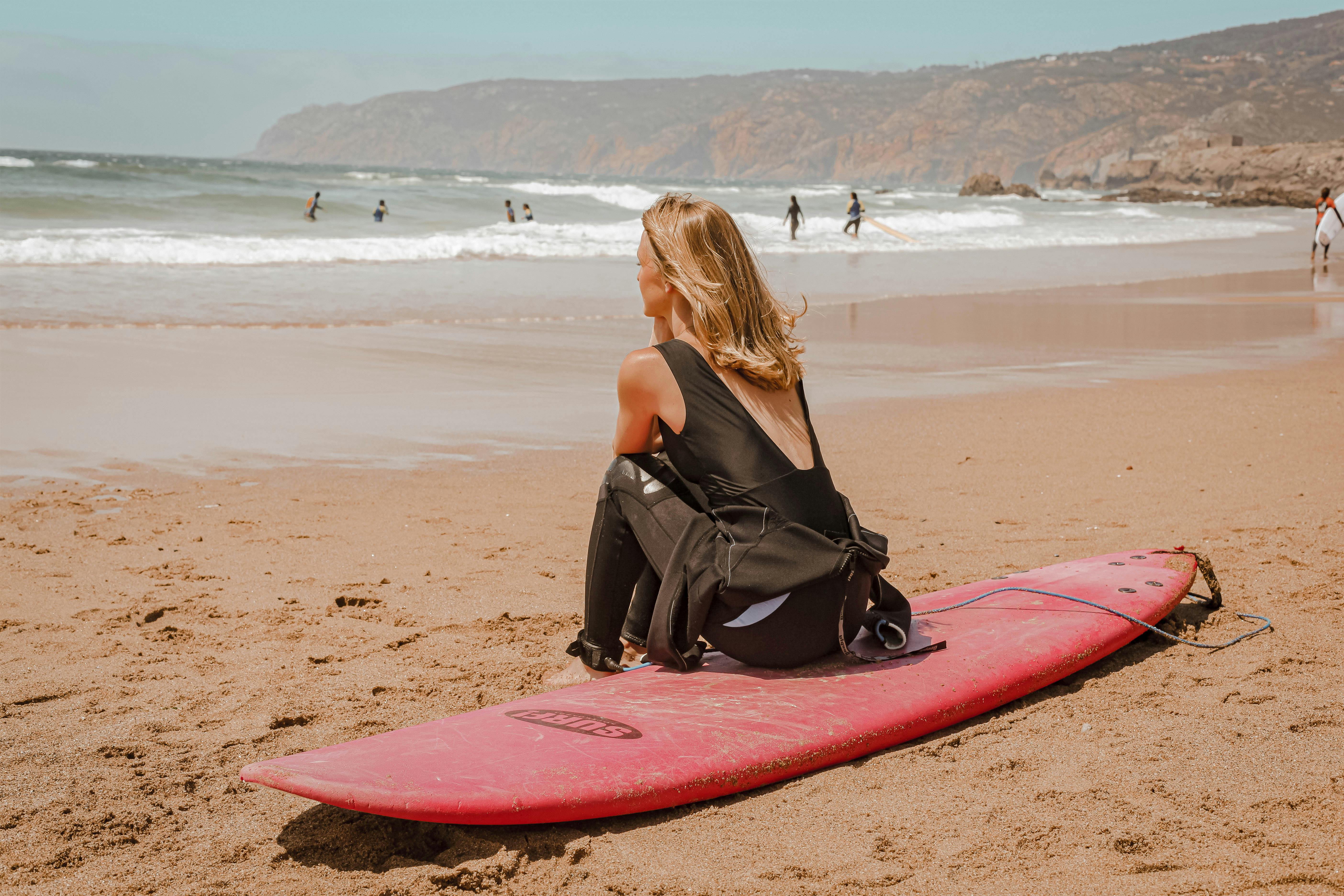 Een persoon die op z'n surfboard zit en over de zee kijkt