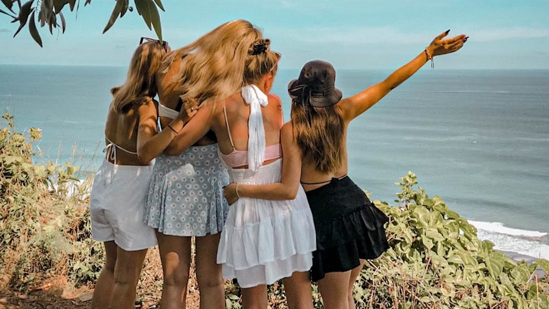 vier Freundinnen die sich umarmen und dabei die Hände in die Luft strecken und auf das Meer blicken