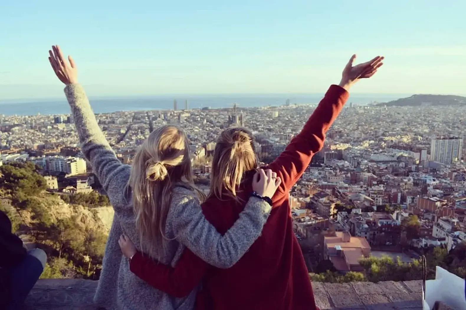 zwei Mädchen umarmen sich und strecken die Arme in die Luft mit Ausblick auf Barcelona