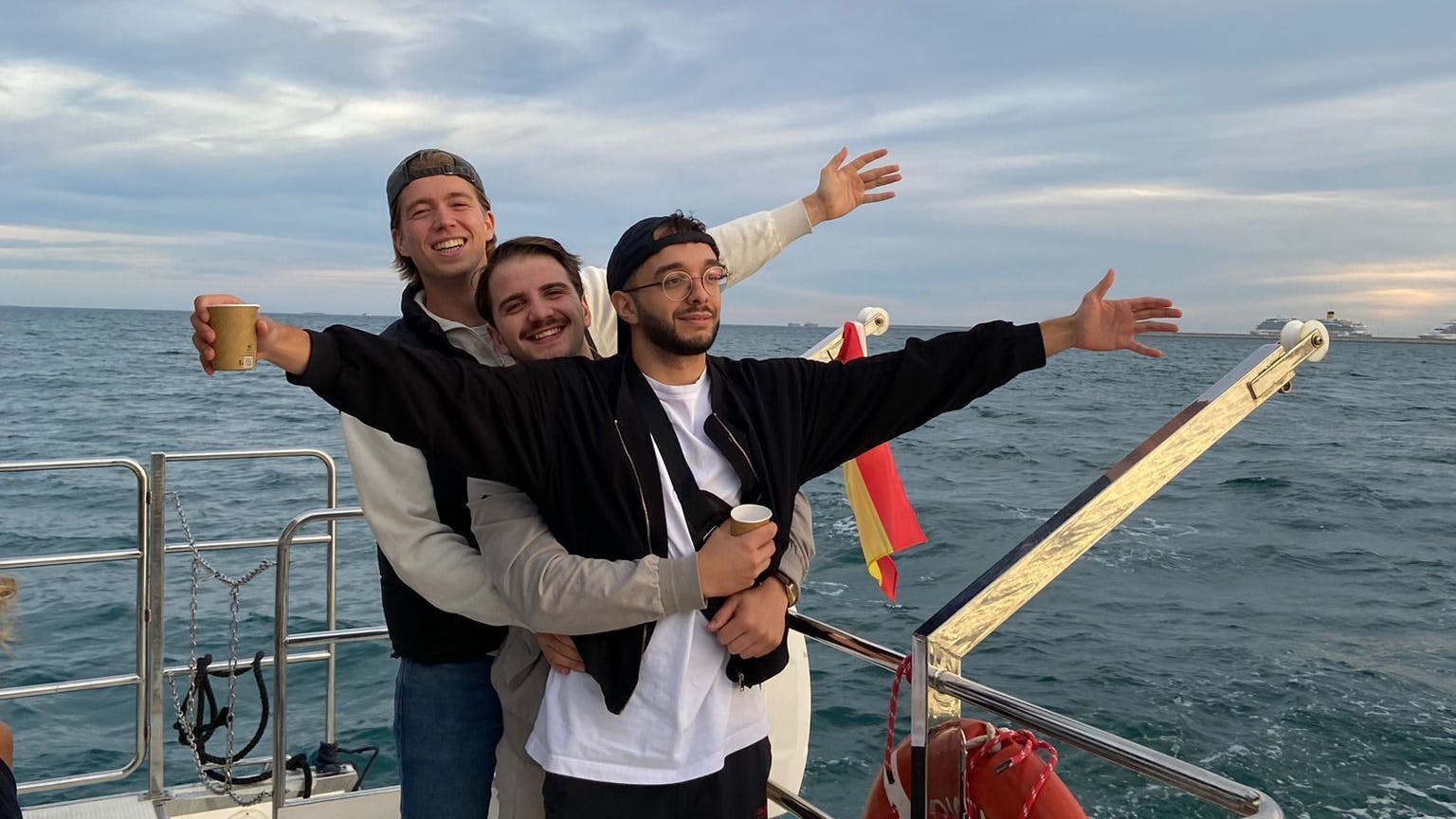 drei Freunde auf einem Boot umarmen sich und strecken die Hände in die Luft