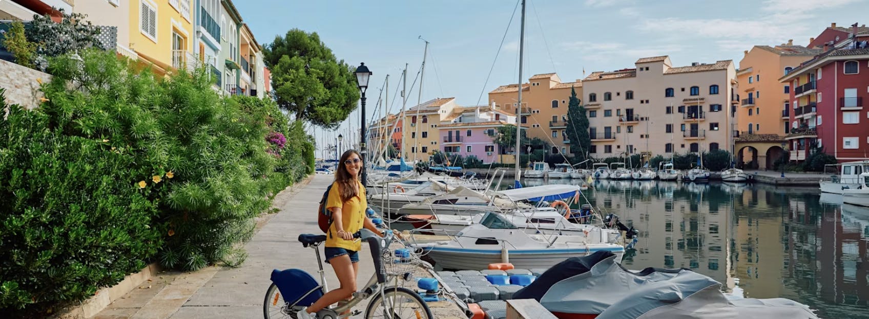 een vrouw lachend met haar fiets in een spaanse stad met boten, water en huisjes